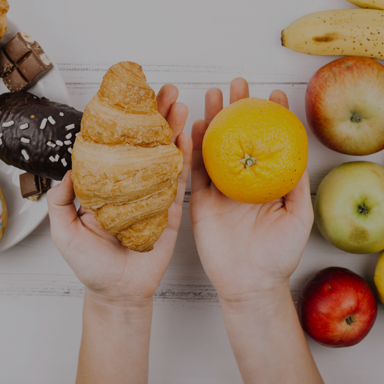 Croissant em uma mão e laranja na outra, representando uma escolha entre alimentação saudável e má alimentação